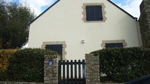 A building with a white facade, two windows with shutters, a stone gate, and a sign indicating the number 5.