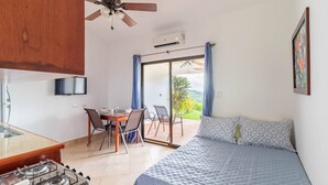 Ein Zimmer mit einem Bett, einem Esstisch mit Stühlen, einer Küchenzeile mit Herd, einem Deckenventilator und Blick durch eine Glastür.