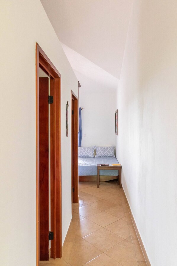 A narrow hallway with wooden doors, a bed with a patterned bedspread, and a small table.