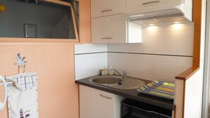 A compact kitchen with white cabinets, a built-in oven, a sink, and a window above the sink.