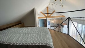 A bedroom with a patterned bedspread, wooden beams, and a view of the living area through a glass partition. - Apartment for 4 sea view near Crouesty port (ARZON)
