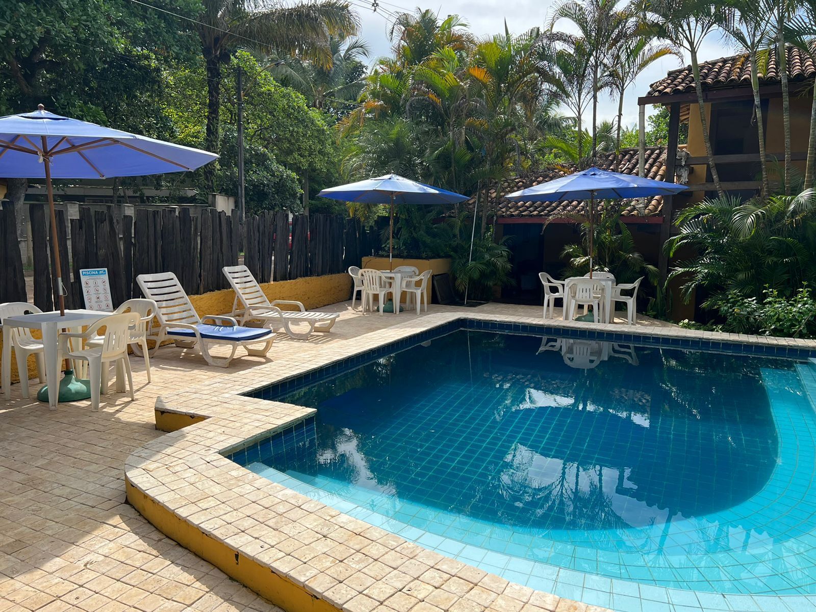 Una piscina con bordes de azulejos, rodeada de sillones de descanso y sombrillas.