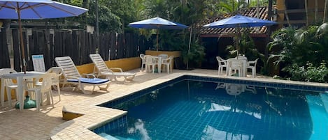 A swimming pool with tiled edges, surrounded by lounge chairs and umbrellas.