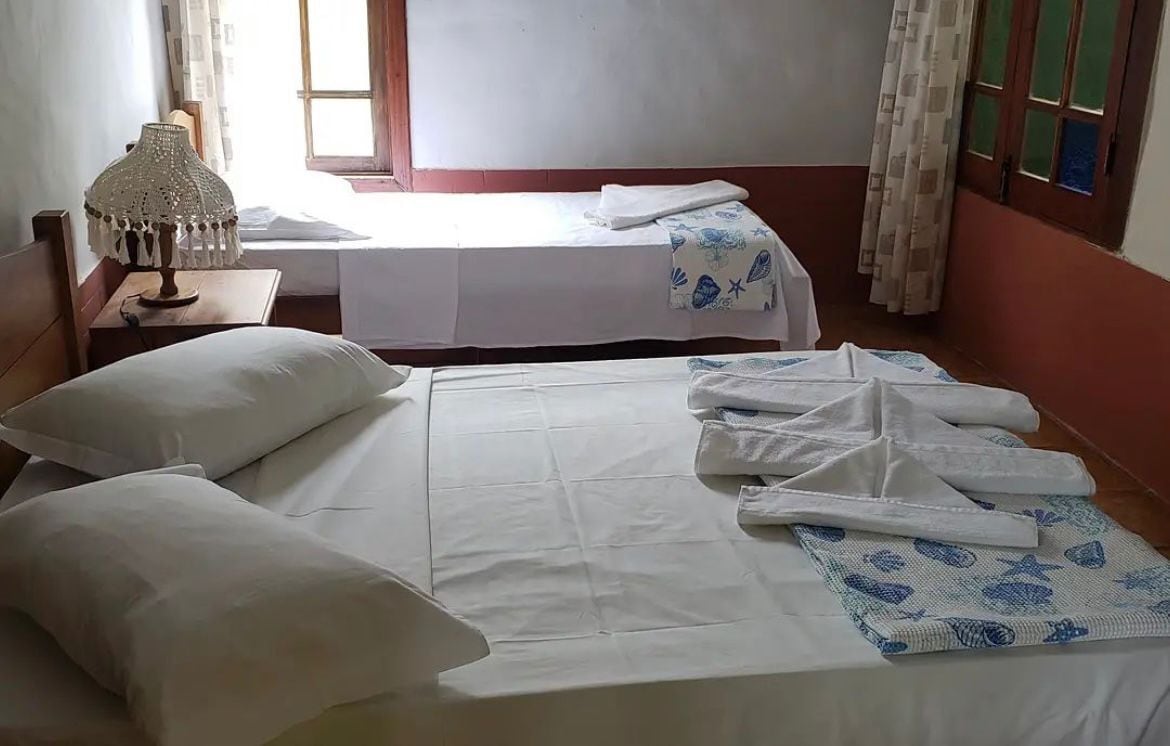 Habitación de hotel con dos camas, una mesita de noche con lámpara y una ventana con cortinas.
