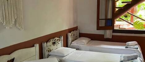 Habitación de hotel con tres camas individuales, un tapiz de macramé y una ventana con vista a vegetación.