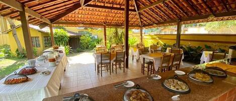 An outdoor dining area with a covered patio, tables set for meals, and a variety of dishes displayed on the counter.