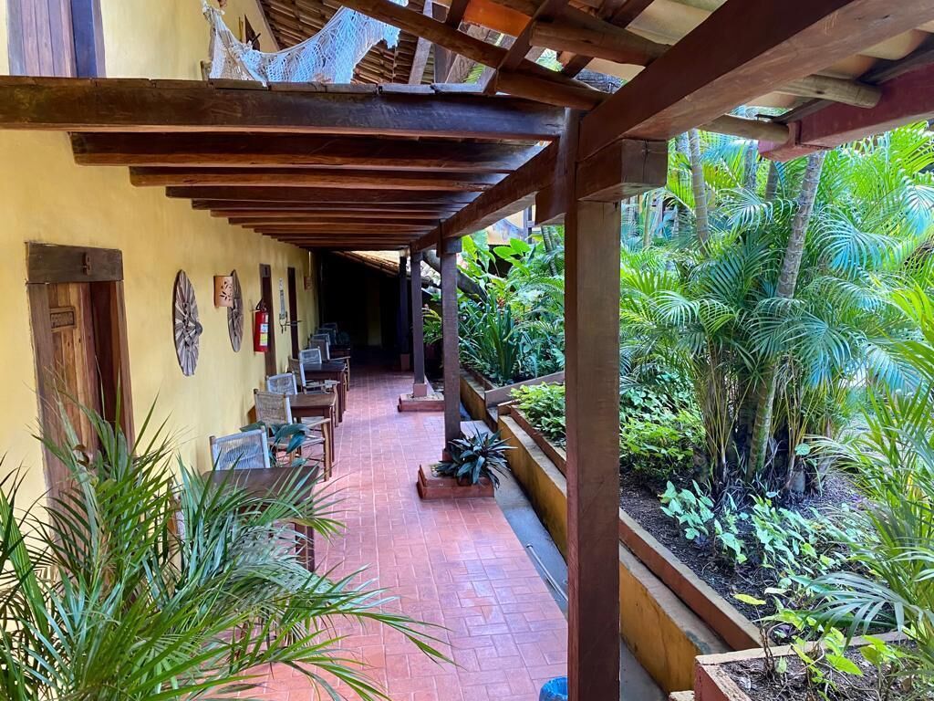 A covered outdoor area with wooden beams, a brick floor, and potted plants.