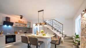 Una cocina moderna con una isla central, taburetes de bar y una escalera con barandilla decorativa.