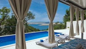 Zona junto a la piscina con vista al mar, una silla de descanso y una mesa con mantel estampado.
