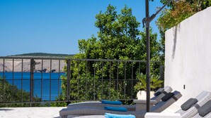 Un salón con sillones de playa y vista al mar, una cerca metálica y una pared blanca.