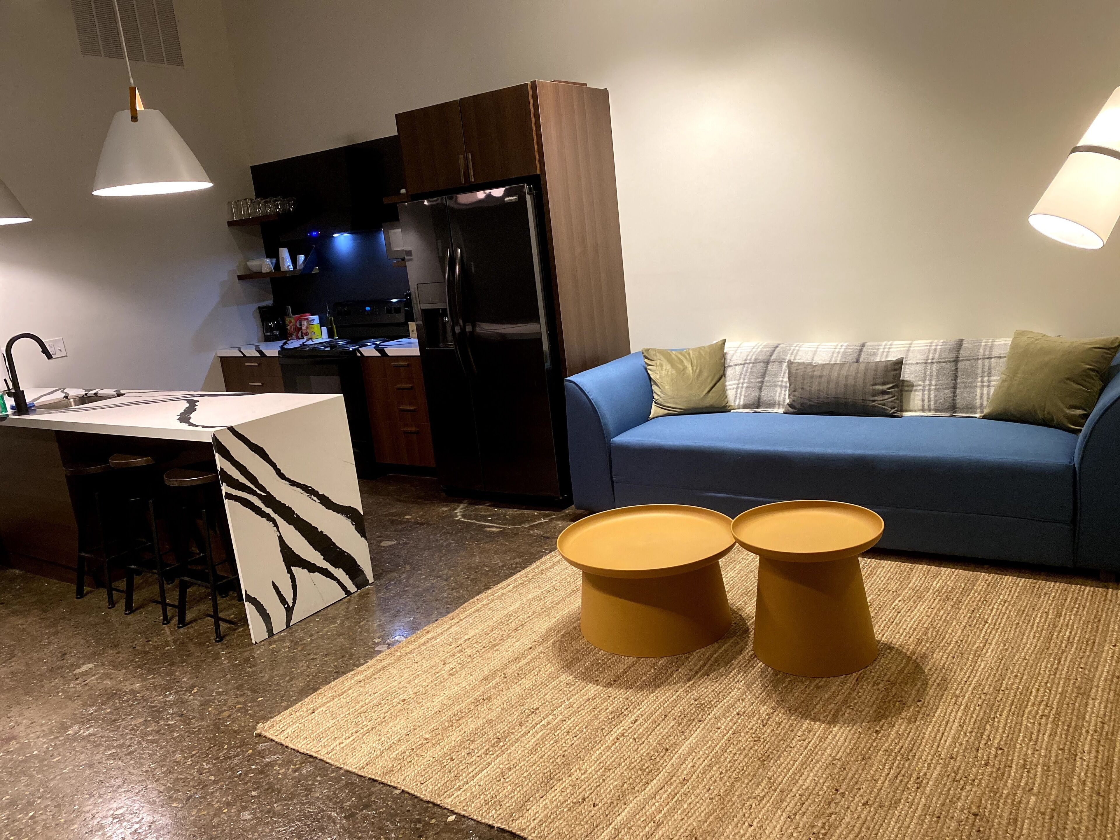 Eine moderne Küche mit Kühlschrank, eine Essecke mit Barhocker und ein blaues Sofa mit Kissen.