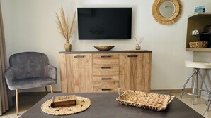 Una sala de estar moderna con una mesa de madera oscura, un sillón gris, un mueble de madera con cajones, un televisor de pantalla plana y un espejo decorativo en la pared.