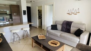 Una sala de estar moderna con un sofá gris, una mesa de centro de madera y una cocina al fondo.