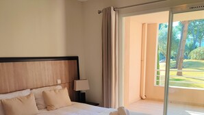 Habitación de hotel con una cama grande, una mesita de noche con lámpara y vistas a un jardín a través de una puerta corrediza de vidrio.