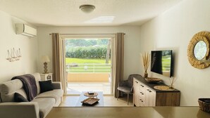 Una sala de estar moderna con sofá, mesa de centro, televisor y vistas a un paisaje verde a través de una puerta corrediza.