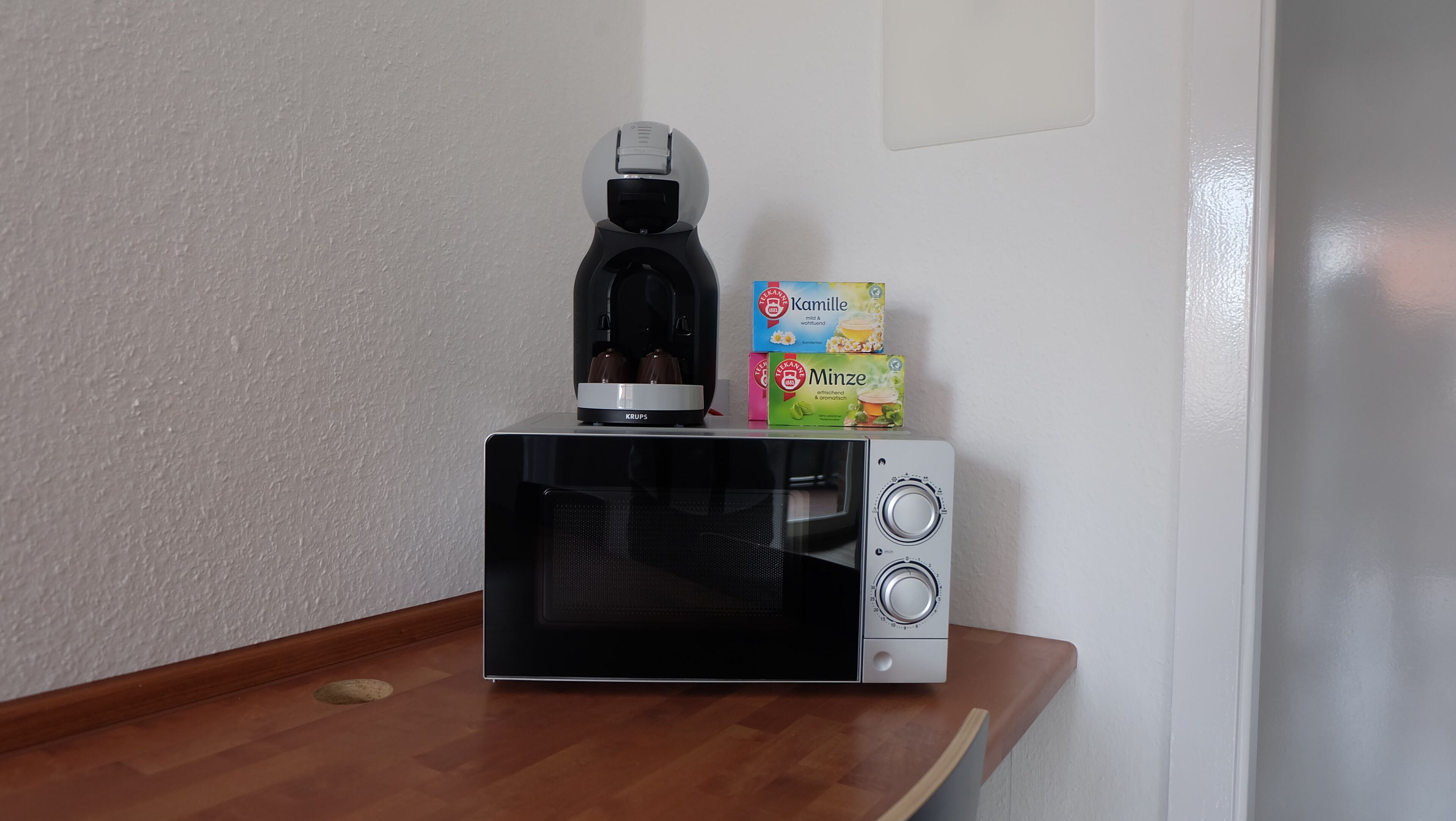 A compact microwave on a wooden countertop with a coffee maker and two boxes of tea.