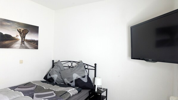 Une chambre à coucher avec un lit, des oreillers, une table de chevet avec une lampe et un téléviseur fixé au mur.
