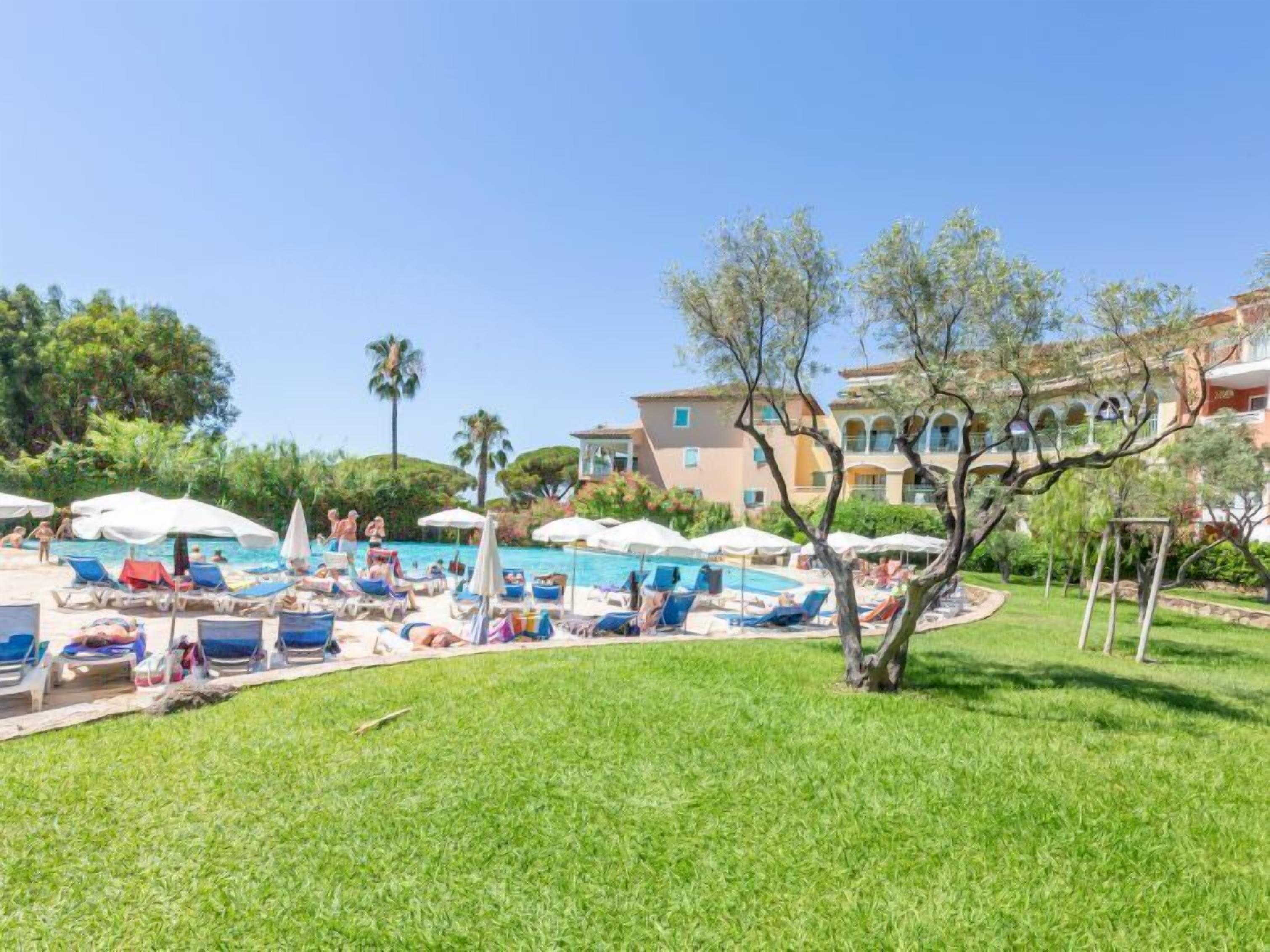 Un'area piscina con lettini e ombrelloni, immersa nel verde e circondata da edifici.