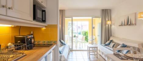 A modern kitchen with a dishwasher, microwave, and coffee machine. There is a dining area with a table and chairs, and a sofa with cushions.