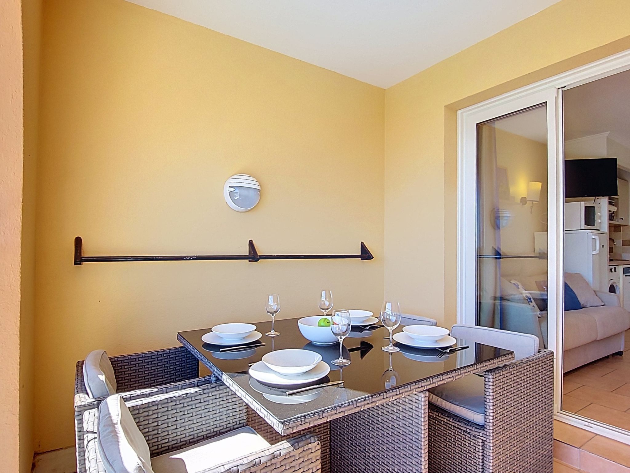 Une table à manger dressée avec des assiettes, des verres et un saladier, entourée de chaises en osier et séparée du reste de la pièce par une cloison en verre.