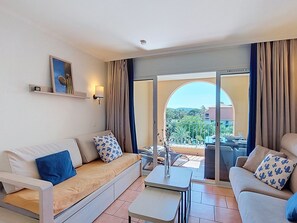 A modern hotel room with a sofa, armchair, and a dining table.