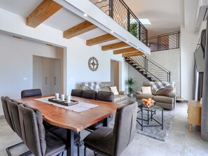 Un espace de vie moderne comprenant un coin repas, des canapés, un escalier et un  élément décoratif mural.