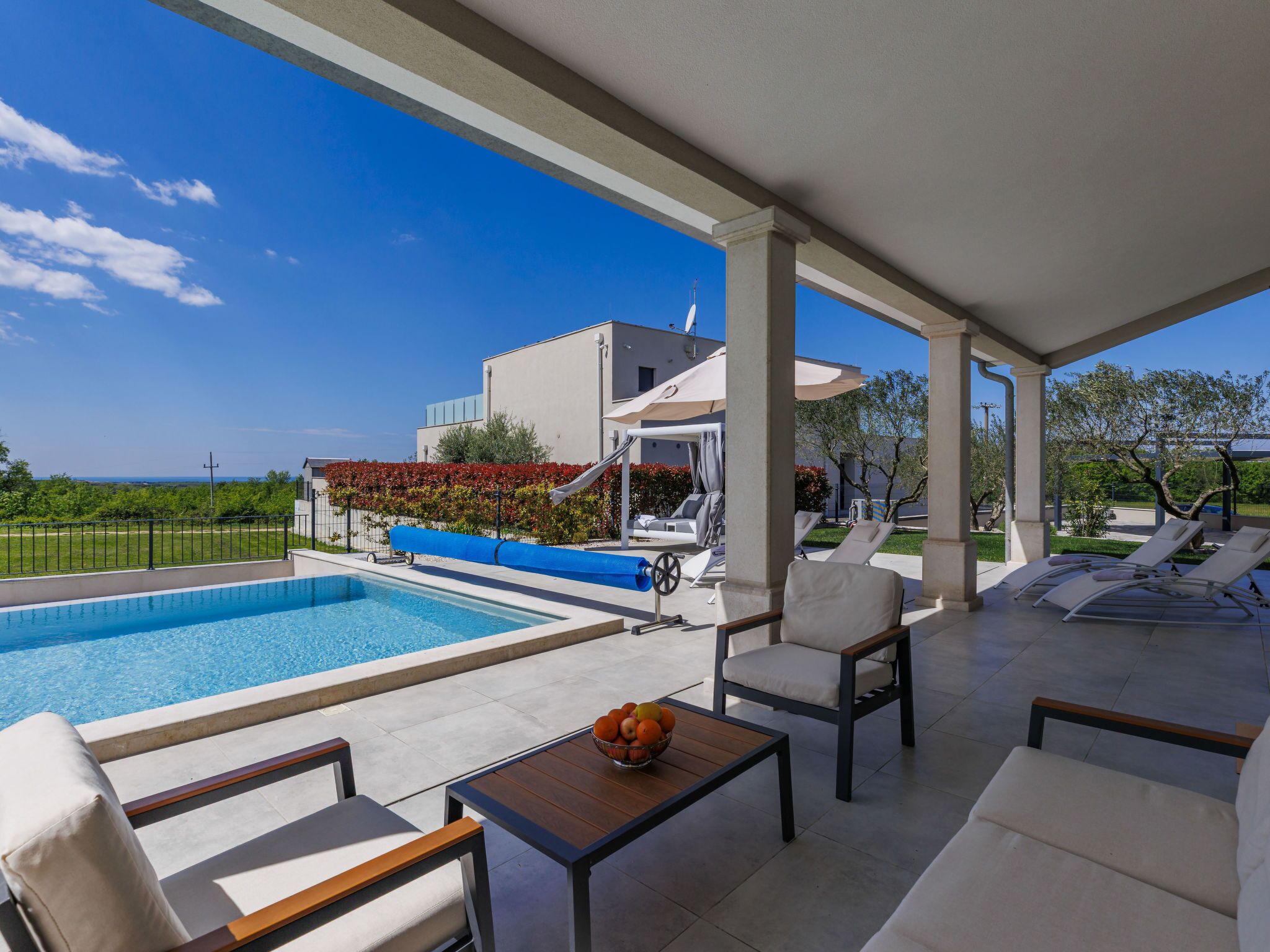 A poolside area with lounge chairs, a table with fruit, and a view of a building and landscape.