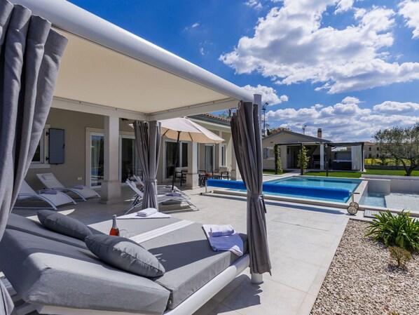 Un espace aménagé au bord de la piscine, avec des chaises longues, une piscine et un patio couvert.