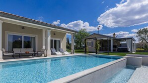 Una piscina con sillas de descanso, un porche cubierto y vistas del paisaje circundante.