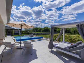 Un espace aménagé au bord de la piscine, comprenant une piscine, des chaises longues et un coin salon abrité.