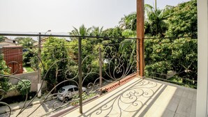 Een balkon met sierijzeren hekwerk, betegelde vloer en uitzicht op een weelderig groen landschap met palmbomen.