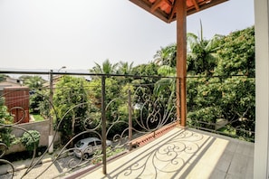 A balcony with wrought iron railings, a tiled floor, and a view of a lush green landscape with palm trees.