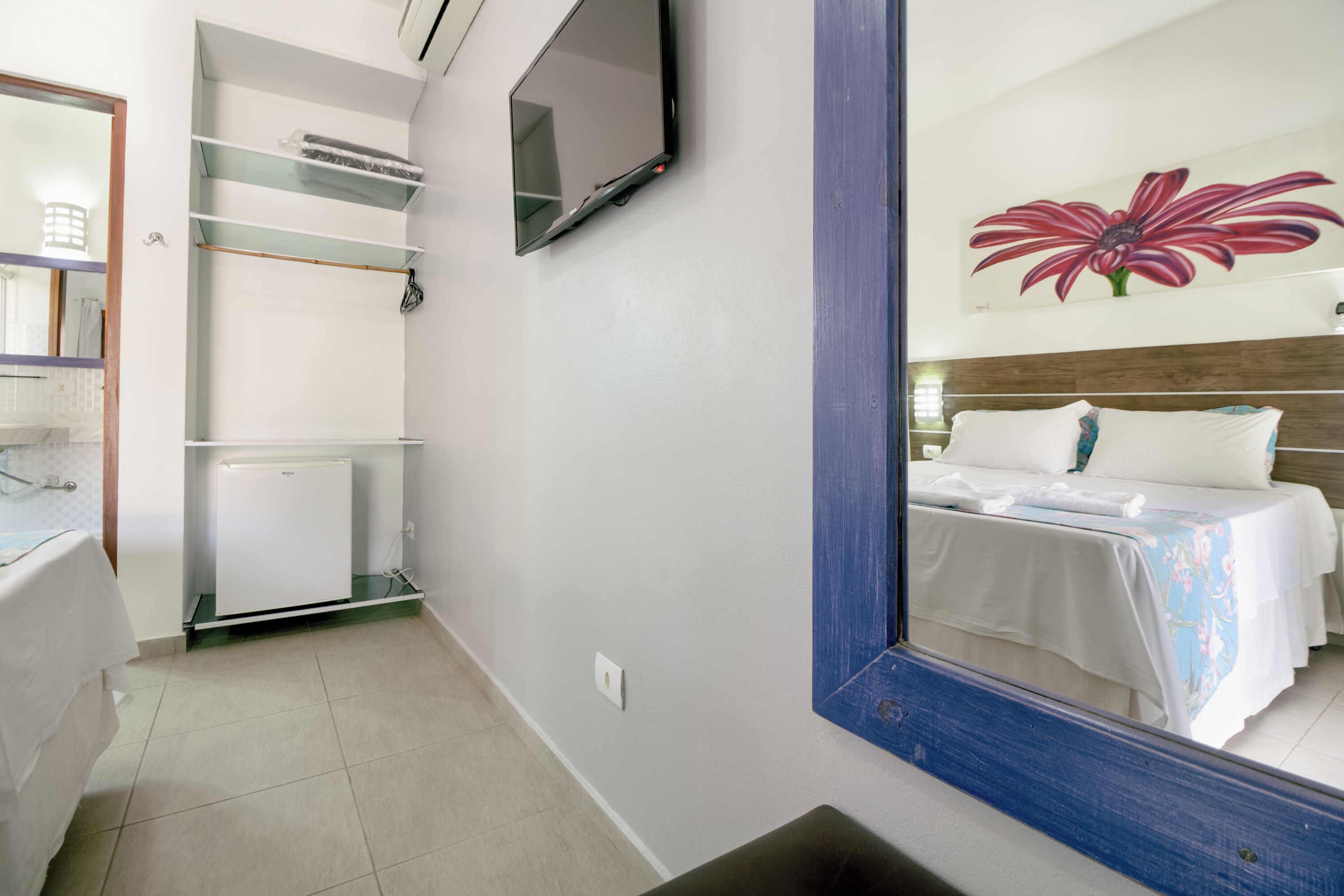 Une chambre d’hôtel avec un lit, un téléviseur fixé au mur, un miroir et un tableau représentant une fleur accroché au mur.