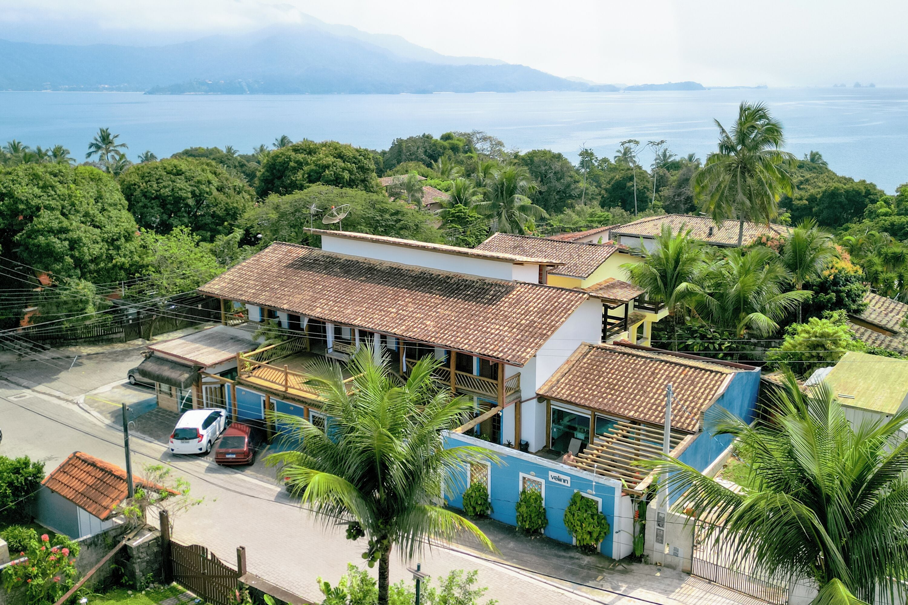 A residential building with a tiled roof, surrounded by lush greenery and a view of the sea.