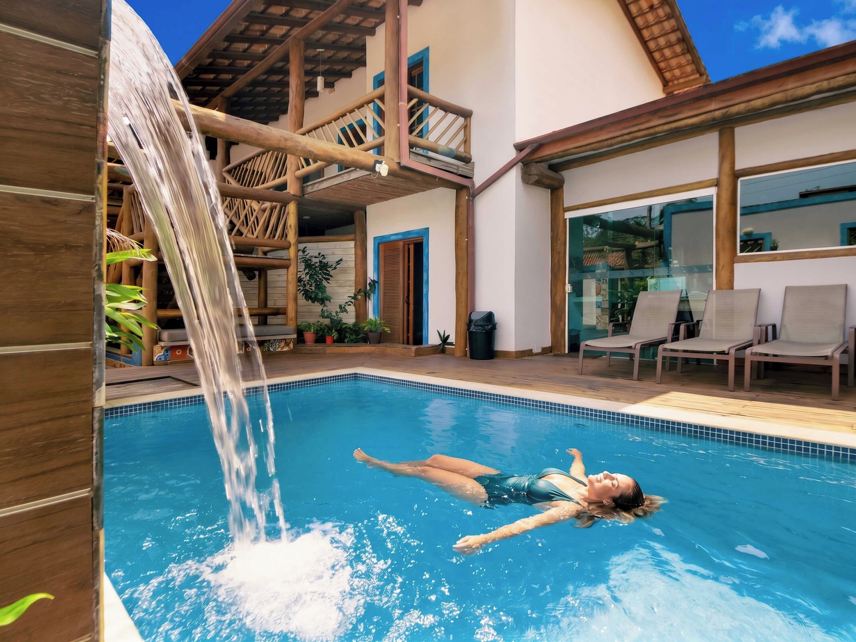 A swimming pool with a waterfall feature, surrounded by wooden deck and lounge chairs.