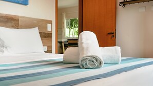 Een net opgemaakt bed met gestreepte lakens, een opgerolde witte handdoek en een houten hoofdbord.