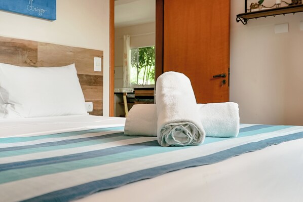 A neatly made bed with striped bedding, a rolled white towel, and a wooden headboard.