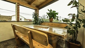 Een houten bank en tafel onder een schuin dak, met plantenpotten.