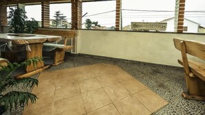 Een overdekt terras met een houten tafel en stoelen, een betegelde vloer en een bakstenen muur.