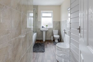 A bathroom with a bathtub, toilet, sink, and a window. - 2-bed House - Sleeps 7 & Free Parking (Barking)