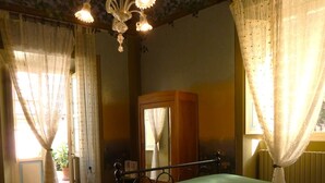 Une pièce comprenant un lit, une table de chevet en bois avec une lampe, un miroir et une porte donnant sur une autre pièce.