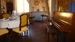 Une salle à manger avec un piano, des chaises en bois, une table dressée pour le repas et un papier peint à motifs.