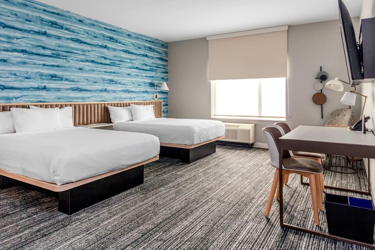A hotel room with two beds, a desk, and a chair.