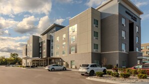 A modern hotel with a flat roof, multiple floors, and a parking lot with several cars. - TownePlace Suites by Marriott Chesterfield (New Baltimore)
