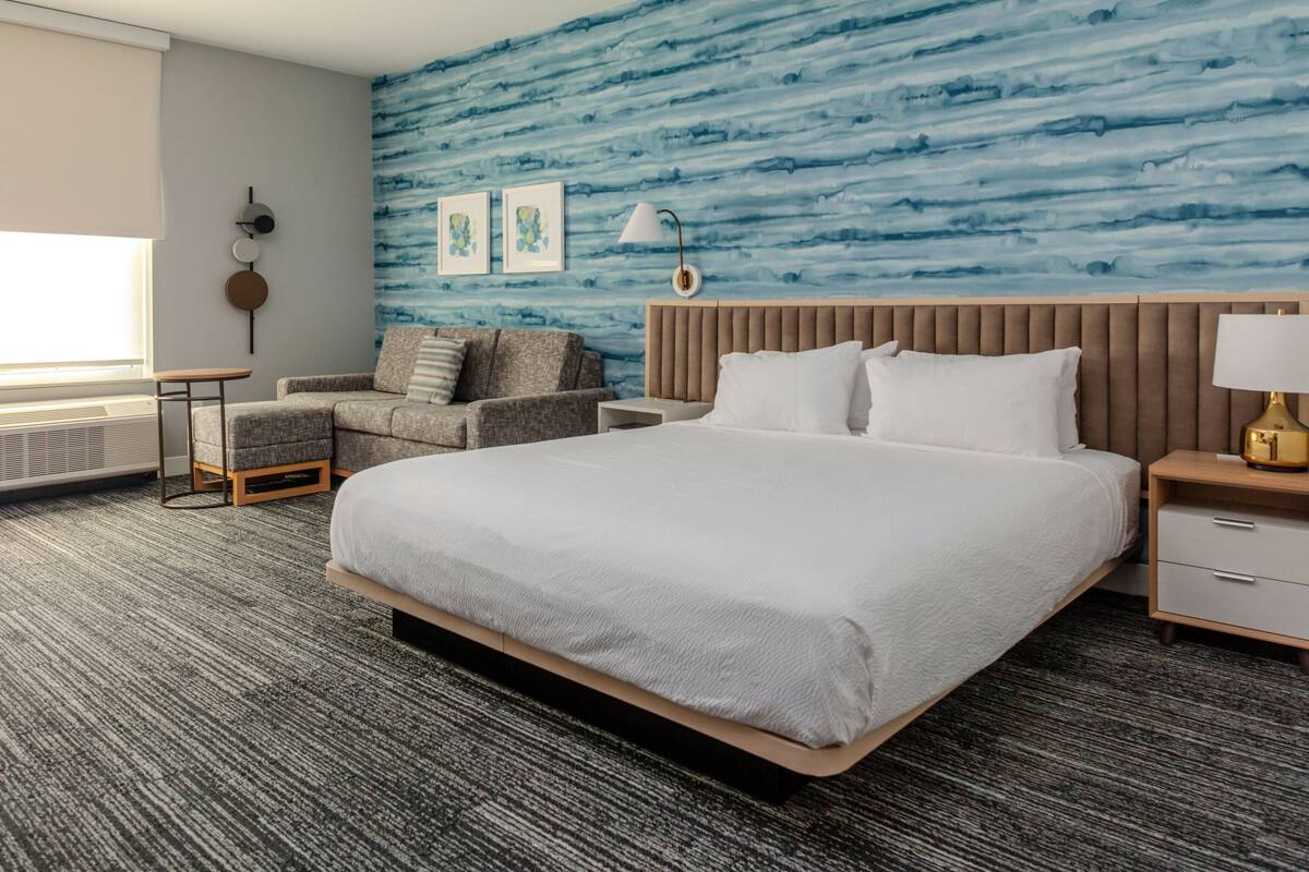 A hotel room with a large bed, a sofa, a small table, and a nightstand.
