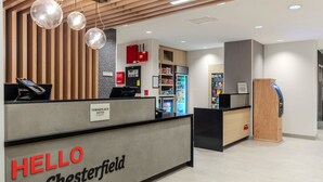 A reception desk labeled "HELLO Chesterfield" with a modern design, including a wooden slat ceiling and pendant lighting. - TownePlace Suites by Marriott Chesterfield (New Baltimore)