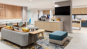 A modern hotel lobby with a sofa, chairs, a small table, a TV, and a kitchen area in the background. - TownePlace Suites by Marriott Chesterfield (New Baltimore)