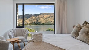 Une chambre avec un grand lit, une chaise, une petite table et une vue sur les montagnes et un lac.