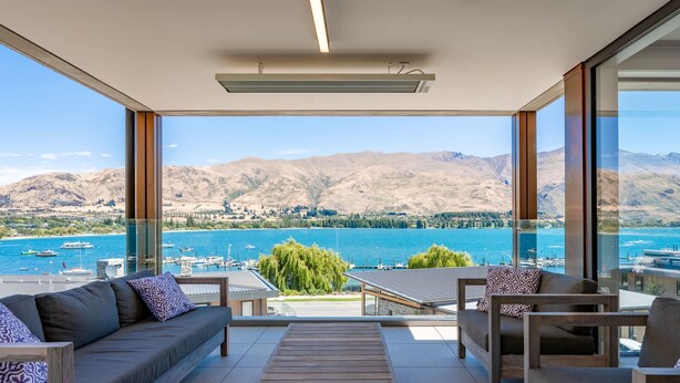 Un balcon agrémenté d’un canapé, de chaises et d’une table, offrant une vue sur un lac et des montagnes.
