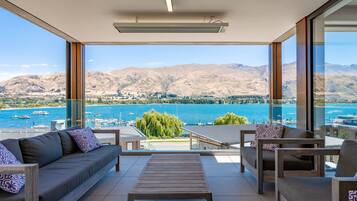A balcony with a sofa, chairs, and a table, overlooking a lake and mountains.